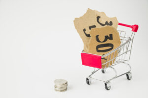 Carrinho de compras com tag's de preços e uma pilha de moedas no chão em frente ao carrinho.